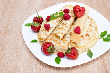 Çilekli ve ahududulu krep. Tabakta ahududu ve çilekli krep. Tabakta ahududu, çilek ve ahşap tahtayla krep..