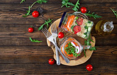 ahşap zemin üzerine salata quinoa, roka, turp, domates ve salatalık cam kavanozlara üstten görünüm