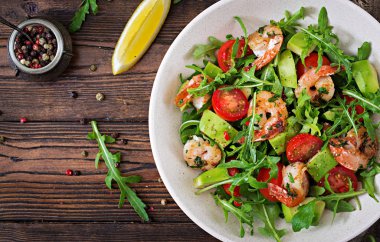 Taze salata kasesi karides, domates, avokado ve roka ahşap zemin üzerine kapatın. Sağlıklı gıda. Temiz yemek. Üstten görünüm.