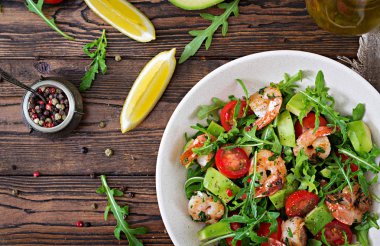 Taze salata kasesi karides, domates, avokado ve roka ahşap zemin üzerine kapatın. Sağlıklı gıda. Temiz yemek. Üstten görünüm.