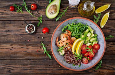 Delicious healthy Buddha bowl with shrimps, tomato, avocado, quinoa, lemon and arugula on the wooden table. Healthy food. Top view clipart