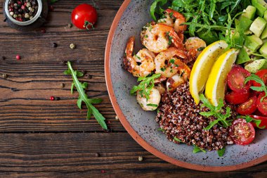 Lezzetli sağlıklı Buda kase karides, domates, avokado, quinoa, limon ve roka ahşap masa üzerinde. Sağlıklı gıda. Üstten görünüm