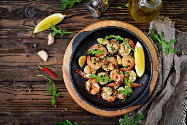 Shrimps roasted in garlic butter with lemon and parsley on wooden background. Healthy food.