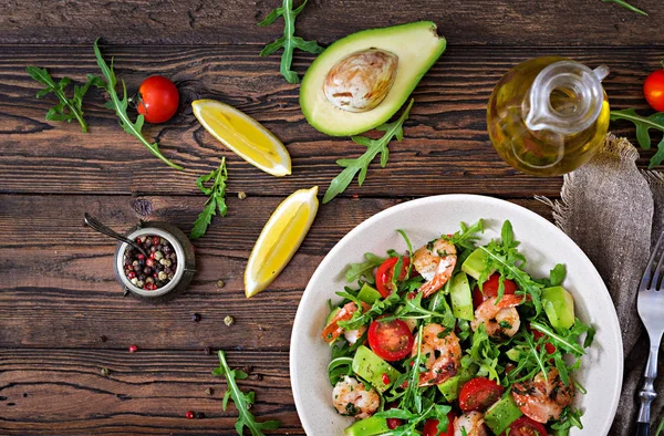 Taze salata kasesi karides, domates, avokado ve roka ahşap zemin üzerine kapatın. Sağlıklı gıda. Temiz yemek. Üstten görünüm.