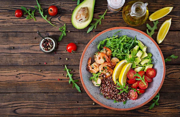 Delicious healthy Buddha bowl with shrimps, tomato, avocado, quinoa, lemon and arugula on the wooden table. Healthy food. Top view — Stock Image Delicious Healthy Buddha Bowl Shrimps Tomato Avocado Quinoa Lemon Arugula Stock Picture