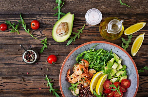 Delicious healthy Buddha bowl with shrimps, tomato, avocado, quinoa, lemon and arugula on the wooden table. Healthy food. Top view — Stock Image Delicious Healthy Buddha Bowl Shrimps Tomato Avocado Quinoa Lemon Arugula Stock Photo