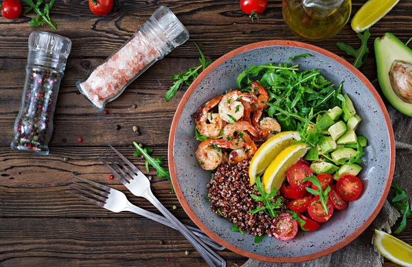 Delicious healthy Buddha bowl with shrimps, tomato, avocado, quinoa, lemon and arugula on the wooden table. Healthy food. Top view — Stock Image Delicious Healthy Buddha Bowl Shrimps Tomato Avocado Quinoa Lemon Arugula Stock Image