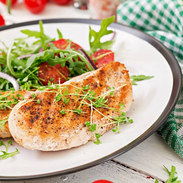 Grilled chicken fillets and fresh vegetable salad of tomatoes, red onion and arugula. Chicken meat salad. Healthy food.