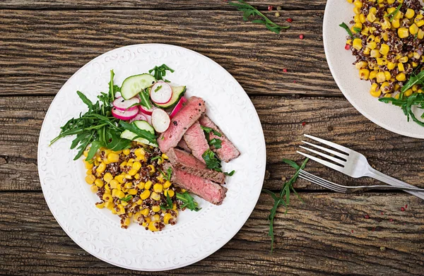 Healthy dinner. Bowl lunch with grilled beef steak and quinoa, corn, cucumber, radishes and arugula on wooden background. Meat salad.