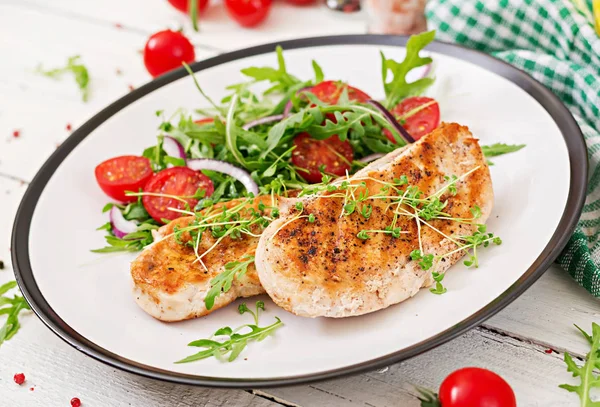 Grilled chicken fillets and fresh vegetable salad of tomatoes, red onion and arugula. Chicken meat salad. Healthy food.