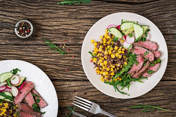 Healthy dinner. Bowl lunch with grilled beef steak and quinoa, corn, cucumber, radishes and arugula on wooden background. Meat salad.