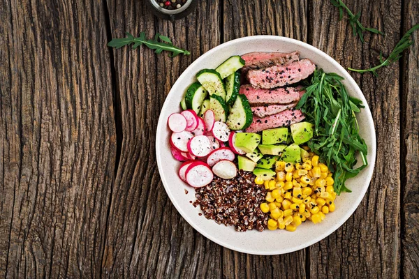 Healthy dinner. Buddha bowl lunch with grilled beef steak and quinoa, corn, avocado, cucumber and arugula on wooden background. Meat salad. Flat lay. Top view