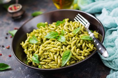Düdük makarna pesto sosu, yeşil bezelye ve fesleğen ile karanlık kapta çatalla hizmet..