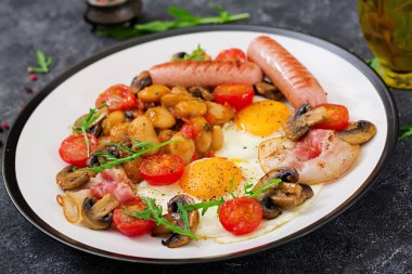 İngiliz kahvaltısı - kızarmış yumurta, fasulye, domates, mantar, pastırma ve sosis görünümü Kapat. 