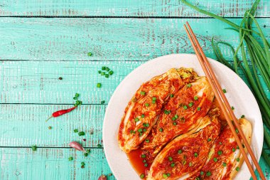 Turkuaz ahşap zemin üzerine Kimchi lahana beyaz plaka üstten görünüm.