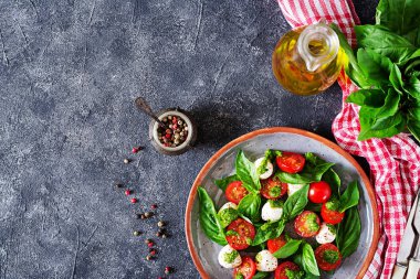 Üstten görünüm Caprese salatası tabağına çatal, bıçak, petrol ve biber, gri masada damalı peçete ile devam eder.