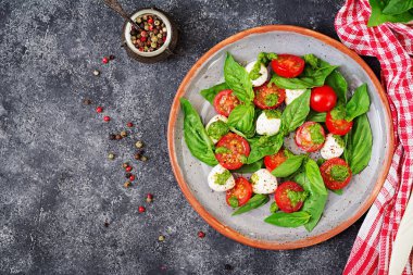 Caprese salatası tabağına gri masada damalı peçete ile servis üstten görünüm.