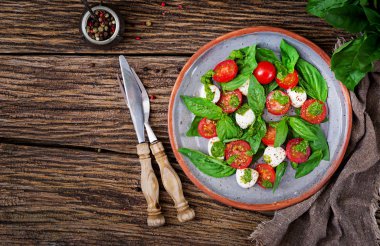 Caprese salatası tabağına çatal ve bıçak ahşap masa üzerinde hizmet üstten görünüm.