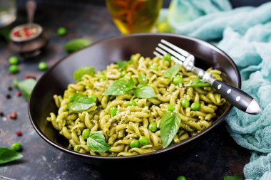 Düdük makarna pesto sosu, yeşil bezelye ve fesleğen ile karanlık kapta çatalla hizmet..