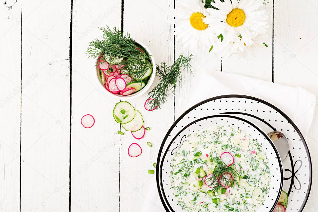 Top view of cold soup with fresh cucumbers, radishes with yoghurt in bowl on wooden background.
