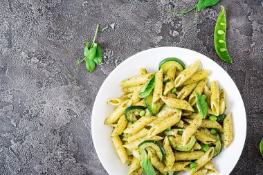 Pesto sos, kabak, yeşil bezelye ve fesleğen gri taş arka penne makarna ile plaka. Kopya alanı ile üstten görünüm
