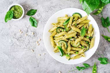Penne makarna ile pesto sos, kabak, yeşil bezelye ve fesleğen beyaz taş zemin üzerine. Kopya alanı ile üstten görünüm