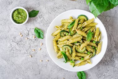 Penne makarna ile pesto sos, kabak, yeşil bezelye ve fesleğen beyaz taş zemin üzerine. Kopya alanı ile üstten görünüm