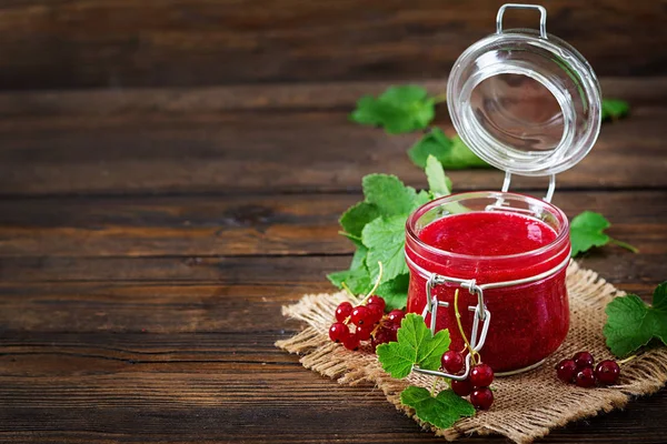 Red currant jam in jar on wooden background with copy space. Tasty food.