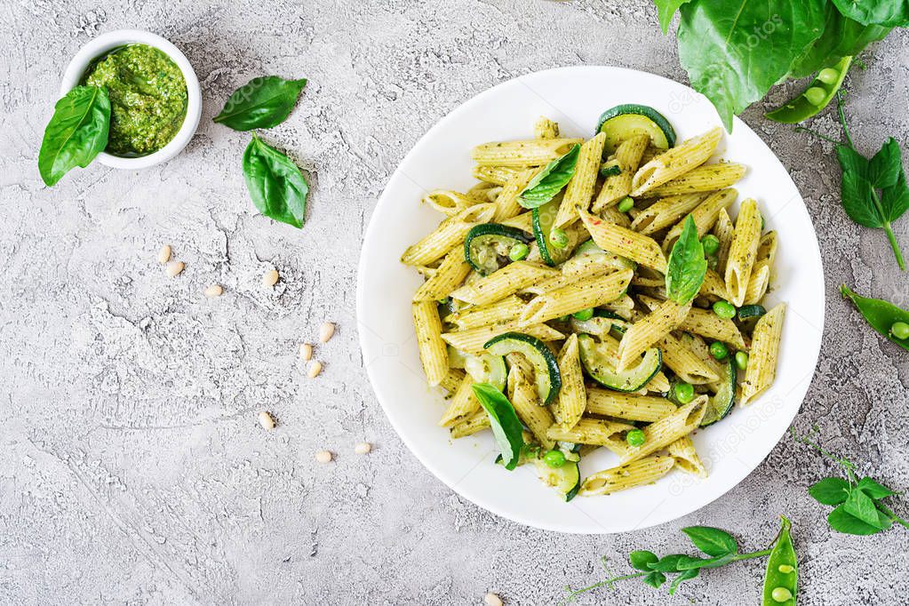 Penne pasta with pesto sauce, zucchini, green peas and basil on white stone background. Top view with copy space