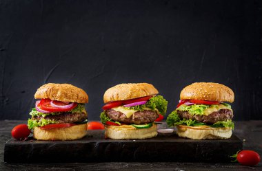 Sığır eti ve taze sebze kopya alanı ile koyu arka plan üzerinde üç hamburger