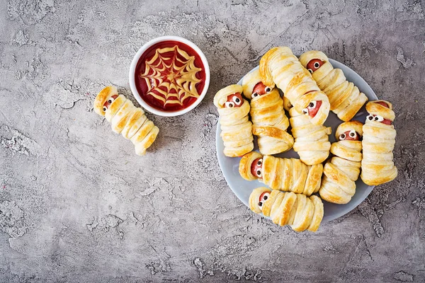 Scary sausage mummies in dough with funny eyes on table. Funny decoration. Halloween food. Top view. Flat lay