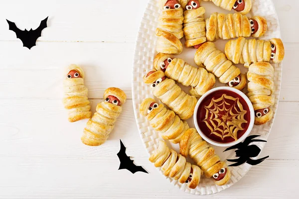 Scary sausage mummies in dough with funny eyes on table. Funny decoration. Halloween food. Top view. Flat lay