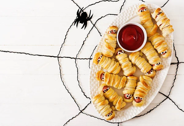 Scary sausage mummies in dough with funny eyes on table. Funny decoration. Halloween food. Top view. Flat lay