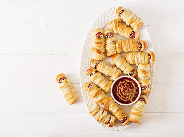 Scary sausage mummies in dough with funny eyes on table. Funny decoration. Halloween food. Top view. Flat lay