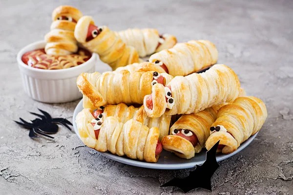 Scary sausage mummies in dough with funny eyes on table. Funny decoration. Halloween food.