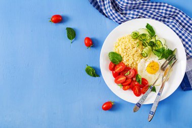 Sağlıklı kahvaltı. Diyet menüsü. Darı yulaf lapası ve domates, salatalık salatası ve sahanda yumurta. Üstten görünüm. Düz yatıyordu