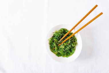 Wakame Chuka veya yosun salatası susam kase beyaz arka plan üzerinde. Geleneksel Japon yemekleri. Üstten görünüm. Düz yatıyordu
