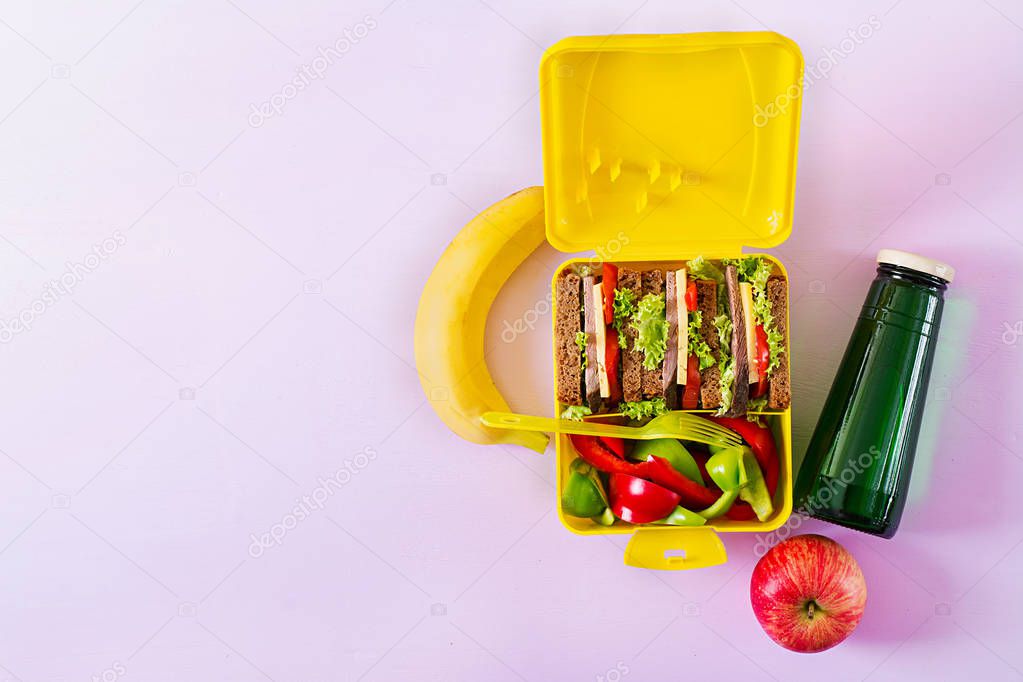 Healthy school lunch box with beef sandwich and fresh vegetables, bottle of water and fruits on pink background. Top view. Flat lay