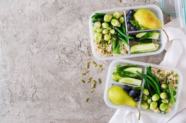 Vegan yeşil yemek hazırlık kapları ile pirinç, fasulye, brussel filizlenir, salatalık ve meyve taş üzerinde arka plan gri