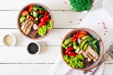 Buddha bowls with chicken fillet, quinoa, avocado, sweet pepper and various vegetables on white table clipart