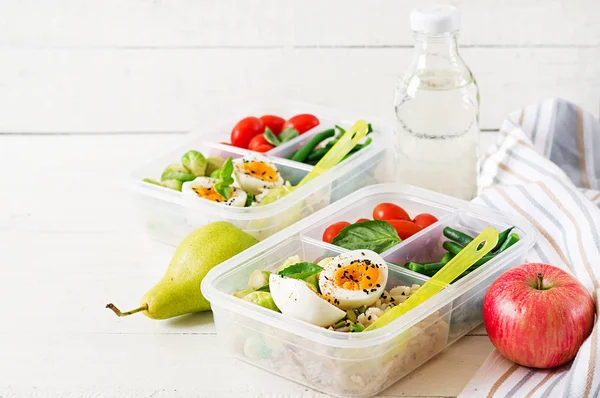 Vegetarian meal prep containers with eggs, brussel sprouts, green beans and tomatoes on white wooden background
