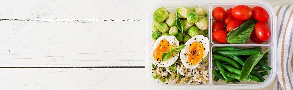 Vegetarian meal prep container with eggs, brussel sprouts, green beans and tomatoes on white wooden background