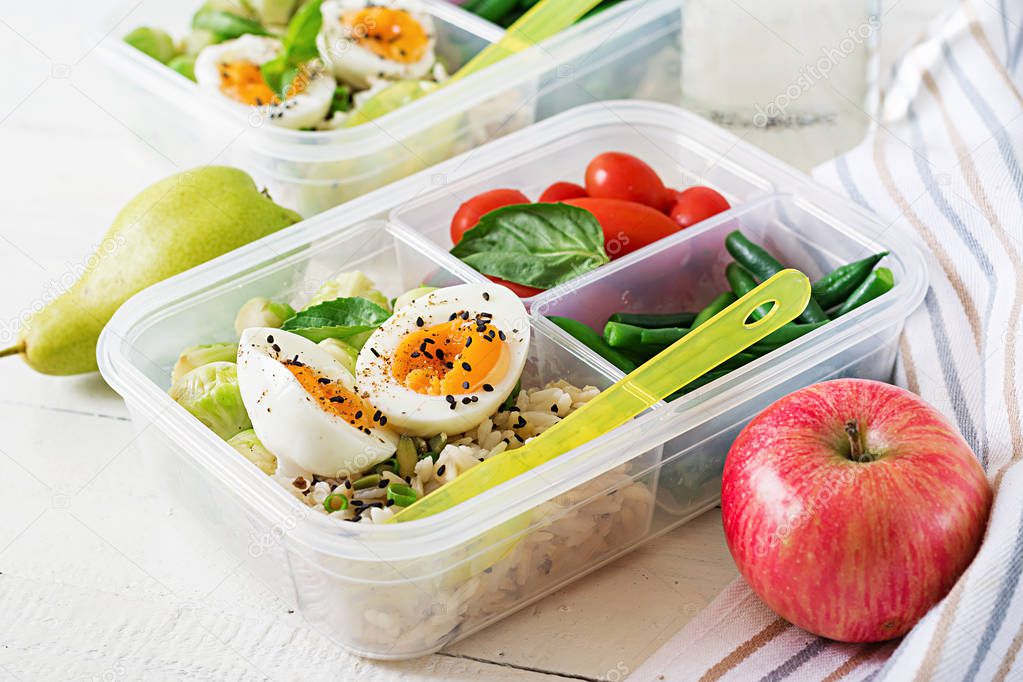 Vegetarian meal prep containers with eggs, brussel sprouts, green beans and tomatoes on white wooden background