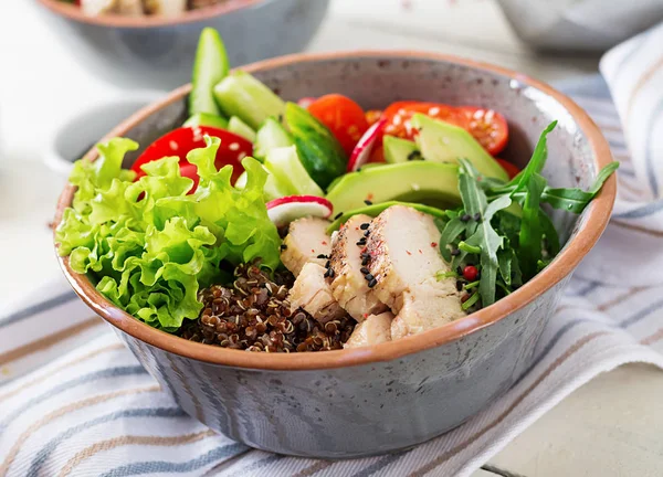 Buddha bowl with chicken fillet, quinoa, avocado, sweet pepper and various vegetables on white table