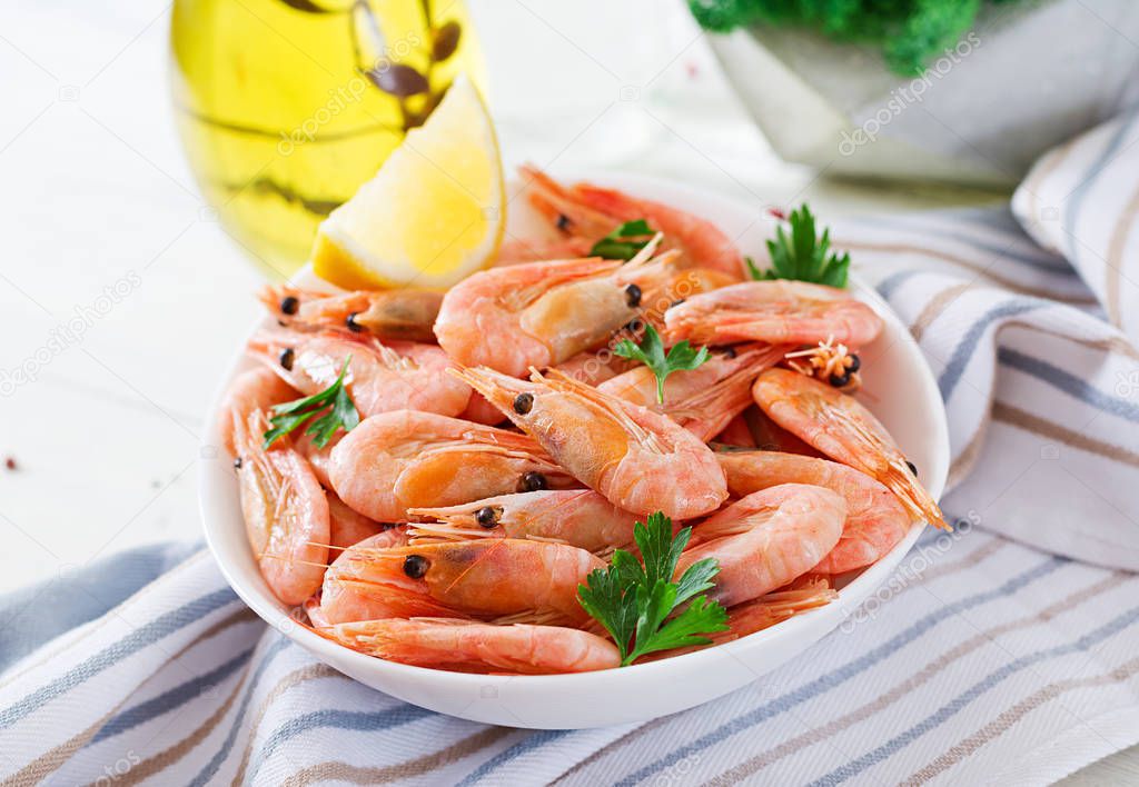 Boiled shrimps in white bowl on striped towel on white table
