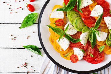 Beyaz ahşap masa üzerinde plaka üzerinde mozzarella peyniri, domates ve fesleğen bitki yaprakları. Caprese salatası. İtalyan yemeği. Üstten görünüm