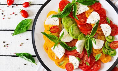 Beyaz ahşap masa üzerinde plaka üzerinde mozzarella peyniri, domates ve fesleğen bitki yaprakları. Caprese salatası. İtalyan yemeği. Üstten görünüm