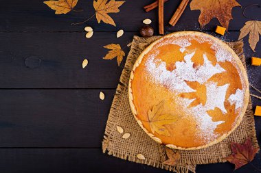 Tarçın ve Hindistan cevizi, kabak çekirdeği ve ahşap bir masa üzerinde sonbahar yaprakları ile dekore edilmiş Amerikan ev yapımı kabak pasta üstten görünüm.