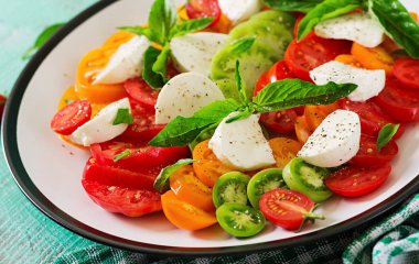 Mozzarella peyniri, domates ve fesleğen bitki tabak içinde beyaz tahta masada bırakır. Caprese salatası. Italyan Mutfagi.