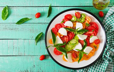 Mozzarella peyniri, domates ve fesleğen bitki, mavi ahşap masa üzerinde beyaz tabak içinde bırakır. Caprese salatası. Italyan Mutfagi.